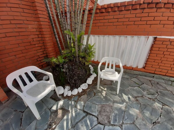 Two white plastic chairs and a small potted plant with white stones in a courtyard with a brick wall and stone flooring.