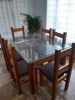 Una mesa de comedor con cubierta de vidrio rodeada de sillas de madera con asientos acolchados.