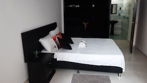 A modern bedroom with a black headboard, white bedding, and a small bedside table with a plant. - Rincon de Granada (Cali)