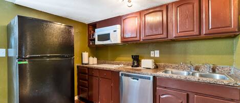 Una cocina con armarios de madera, un refrigerador negro, microondas, cafetera y lavavajillas.