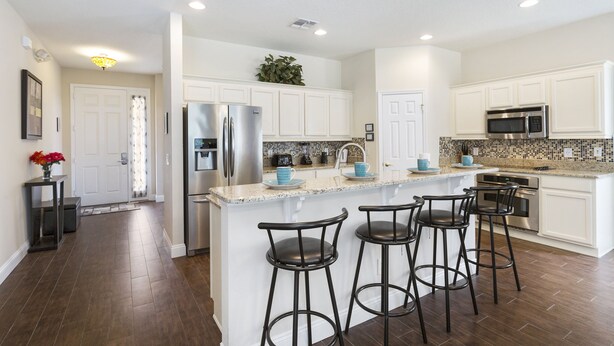A modern kitchen with white cabinets, stainless steel appliances, and a central island with bar stools. - Fantasy Villa by VillaDirect (Kissimmee)