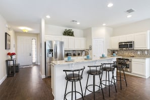 A modern kitchen with white cabinets, stainless steel appliances, and a central island with bar stools. - Fantasy Villa by VillaDirect (Kissimmee)