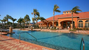 A swimming pool with a tiled deck, palm trees, and a building with arches and a red roof. - Fantasy Villa by VillaDirect (Kissimmee)