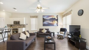 A modern living room with a sofa, coffee table, TV stand, and a painting of a lake. - Fantasy Villa by VillaDirect (Kissimmee)