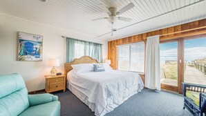 Une chambre à coucher avec un lit, un ventilateur de plafond, une table de chevet, une lampe, une chaise et une vue sur l’extérieur.