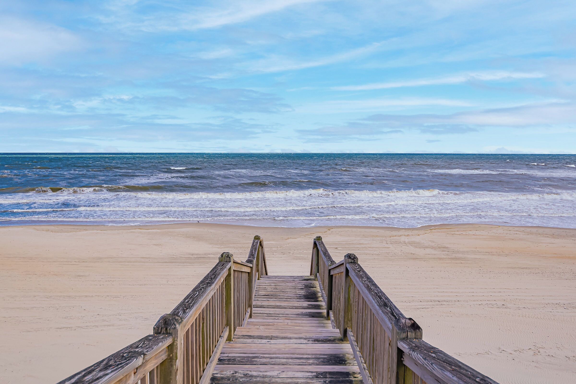 A wooden boardwalk leading to a beach with waves in the background.