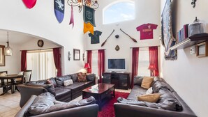 A living room with leather sofas, a coffee table, a TV, and red curtains. Flags and a coat rack are on the walls. - Harrys Hide Out by VillaDirect (Kissimmee)