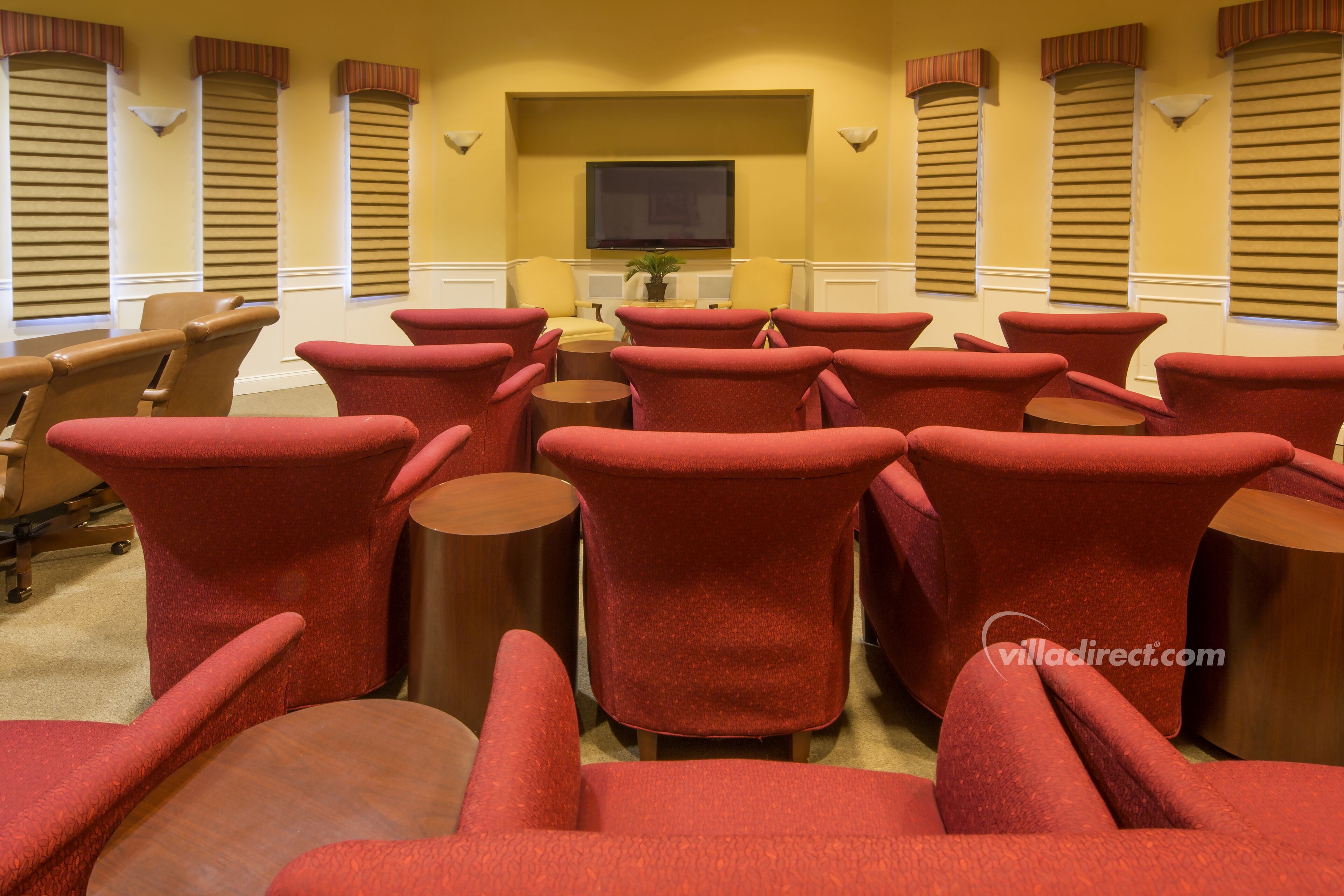 A conference room with red chairs and a round table, a television on the wall, and a plant on the table.