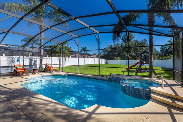 A covered swimming pool with a hot tub, surrounded by lounge chairs and a slide.