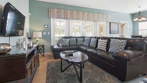 A living room with a sectional sofa, a glass coffee table, a flat-screen TV, and a dark wood cabinet. - Mickey Haven by VillaDirect (Kissimmee)