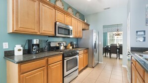 A kitchen with wooden cabinets, stainless steel appliances, and a tiled floor. - Mickey Haven by VillaDirect (Kissimmee)