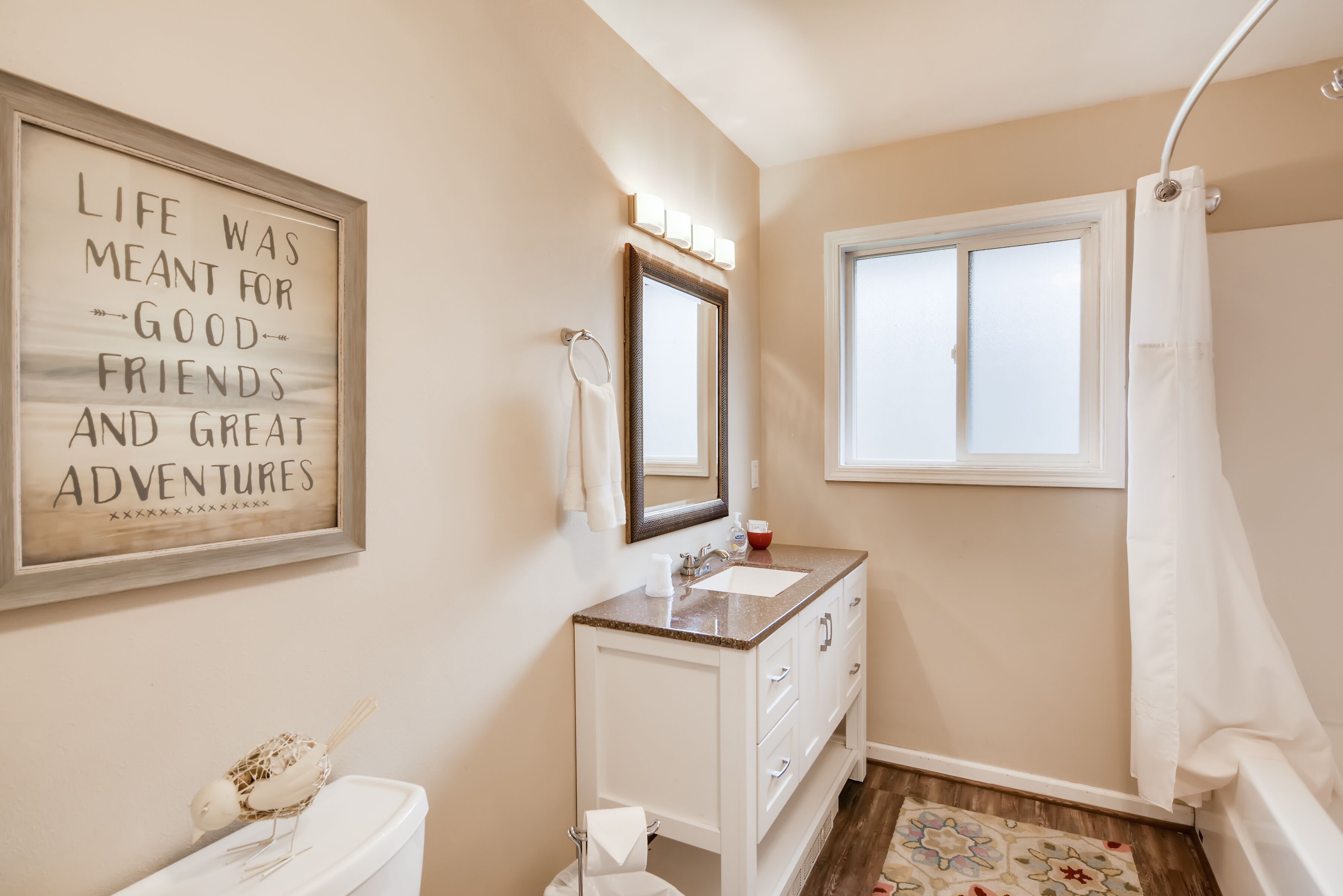 A bathroom with a vanity, a toilet, a mirror, a towel rack, a shower curtain, and a window.