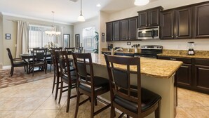 A modern kitchen with dark wood cabinets, a granite countertop, and a dining area with a table and chairs. - Paradise Getaway by VillaDirect (Kissimmee)