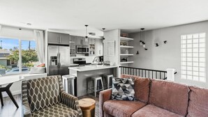 A modern kitchen with stainless steel appliances, a dining area with patterned chairs, and a cozy living space with a pink sofa.