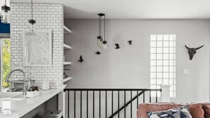 A modern kitchen with white brick backsplash, hanging pendant lights, and a black railing.