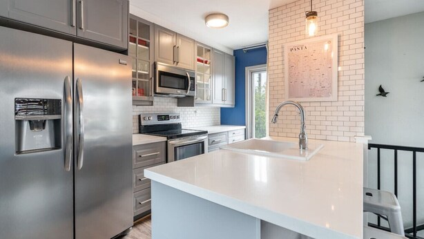 A modern kitchen with stainless steel appliances, a white island with a sink, and a brick accent wall.