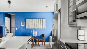 A modern kitchen with a blue accent wall, stainless steel appliances, and a dining area with a round table and chairs.