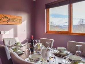 A dining room with a table set for four, a window with a mountain view, and a wall-mounted painting. - 3 bedroom accommodation in Banavie, near Fort William (Banavie, near Fort William)