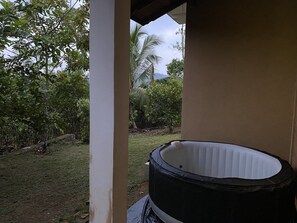 A hot tub in a covered outdoor area with a view of a garden and trees.