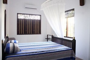 A bedroom with a bed, a window with a curtain, a wall-mounted air conditioner, and a window with decorative bars.