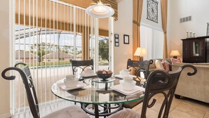 A dining area with a glass table, metal chairs, and a view of a swimming pool. - Timeless Memories by VillaDirect (Kissimmee)