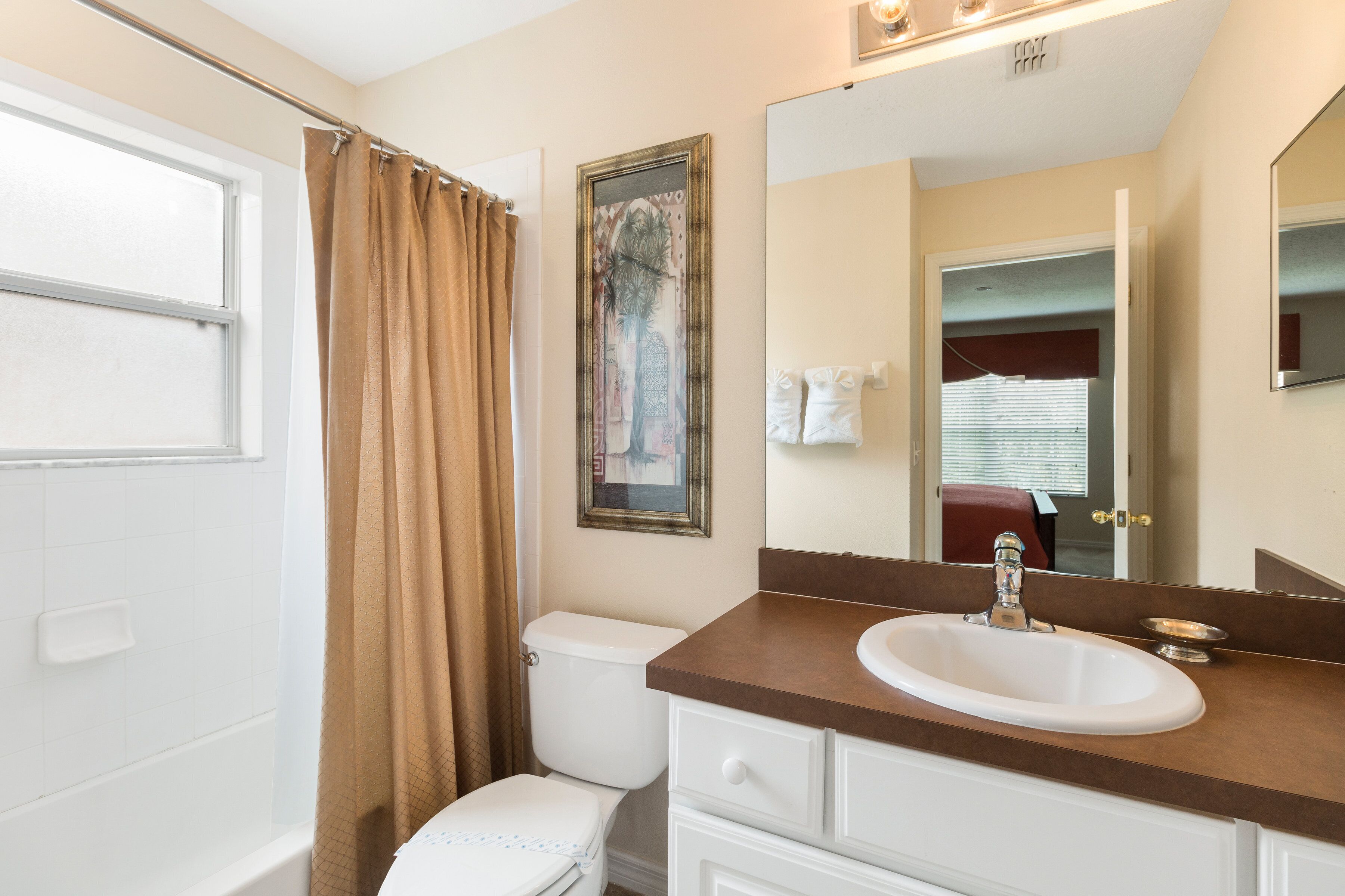 A bathroom with a white toilet, a brown shower curtain, a sink with a mirror above it, and a framed artwork on the wall.