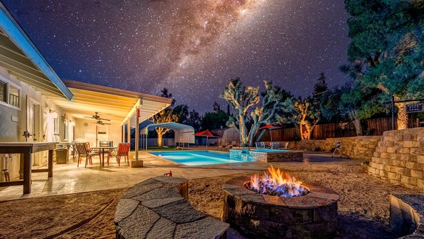 Un patio trasero con piscina, una fogata y un área de patio techada.
