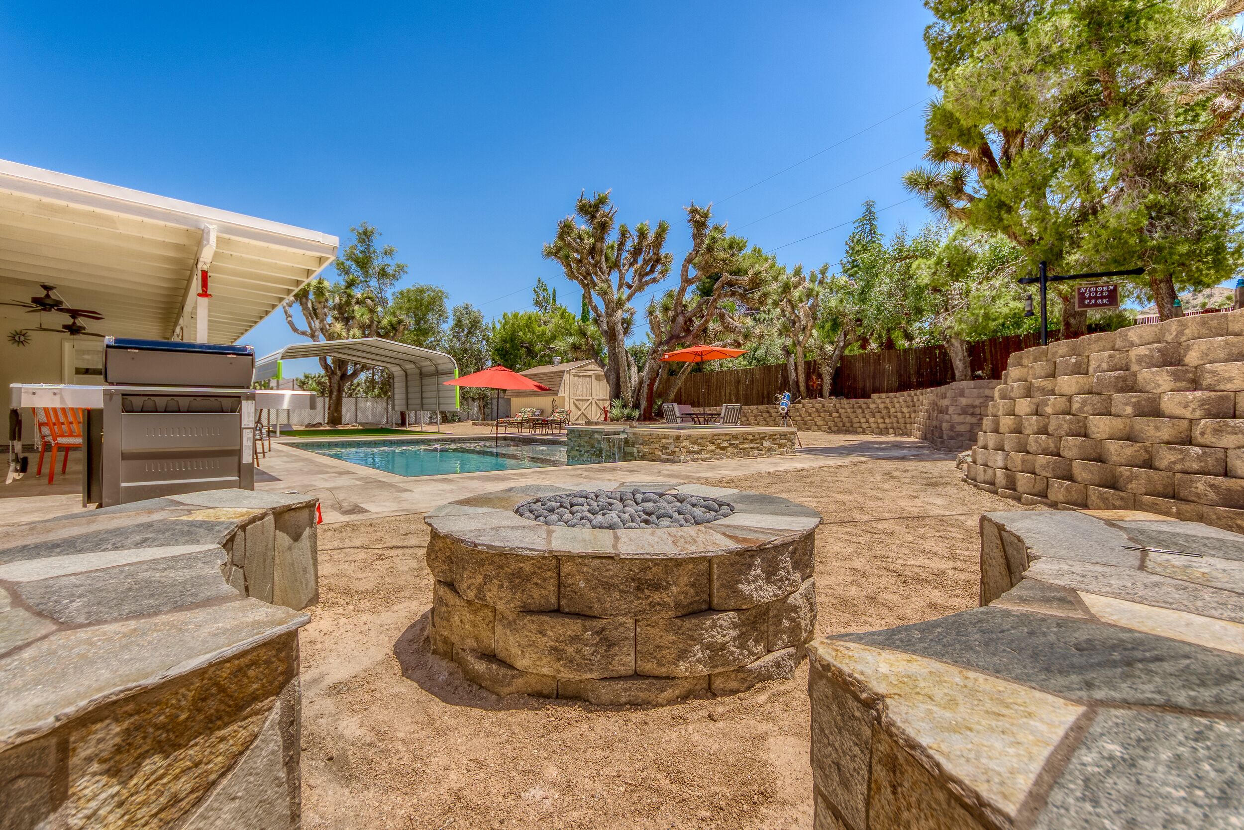 Un jardin avec un foyer en pierre, une piscine, du mobilier d’extérieur et un patio couvert.