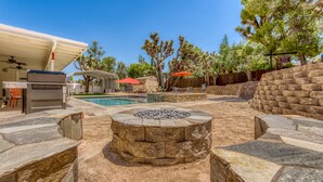 Un patio trasero con un hogar de piedra, una piscina, mobiliario exterior y un área de patio techada.
