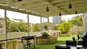 An outdoor patio area with a covered seating area, a brick planter with plants, and a view of surrounding buildings. - Gold Coast Inn (Surfers Paradise)