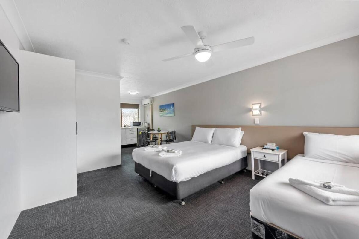 Habitación de hotel con dos camas, un escritorio, una silla, un ventilador de techo y una lámpara en la pared.
