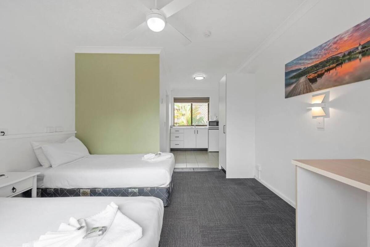 Una habitación de hotel con dos camas, un kitchenette y un baño visible a través de una puerta abierta.