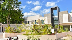 A modern building with a geometric facade, a large glass entrance, and a landscaped garden area with various plants. - Waye Valladolid Centro – Sustainable, Authentic Experiences & Pet Friendly Boutique Hotel (Valladolid)