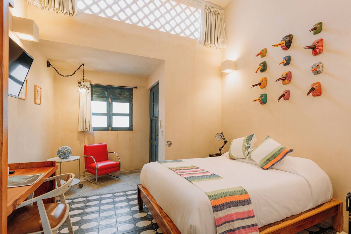 A bedroom with a bed, a desk, a chair, a window, and wall art.