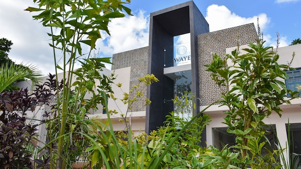 A modern hotel with a geometric facade, a prominent entrance, and lush greenery in the foreground. - Waye Valladolid Centro – Sustainable, Authentic Experiences & Pet Friendly Boutique Hotel (Valladolid)