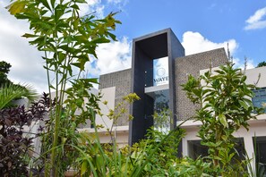 Een modern hotel met een geometrisch gevelontwerp, een opvallende ingang en weelderige beplanting op de voorgrond.