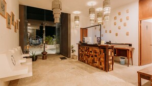 A reception area with a wooden reception desk, multiple pendant lights, framed artwork on the wall, and a potted plant. - Waye Valladolid Centro – Sustainable, Authentic Experiences & Pet Friendly Boutique Hotel (Valladolid)