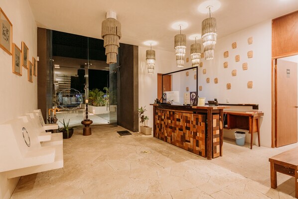 Un área de recepción con un mostrador de madera, varias lámparas colgantes, obras de arte enmarcadas en la pared y una planta en maceta.