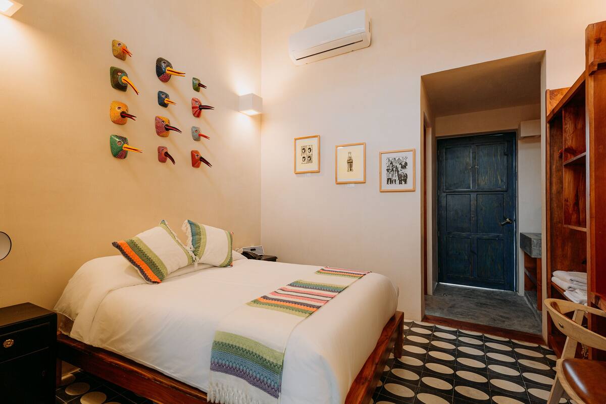 A neatly arranged bedroom with a bed, a wall-mounted bird decoration, a door, and a small wooden chair.