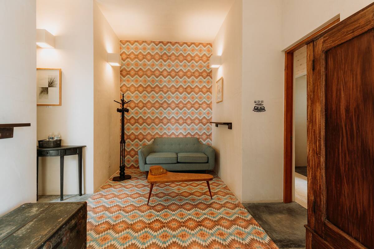 A hallway with a patterned carpet, a sofa, a small table, and a wooden door.