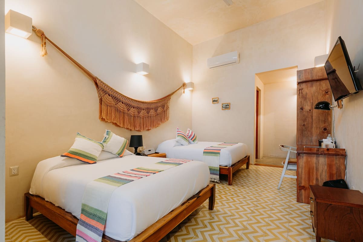 A hotel room with two beds, a wooden desk, a television, and a hammock.