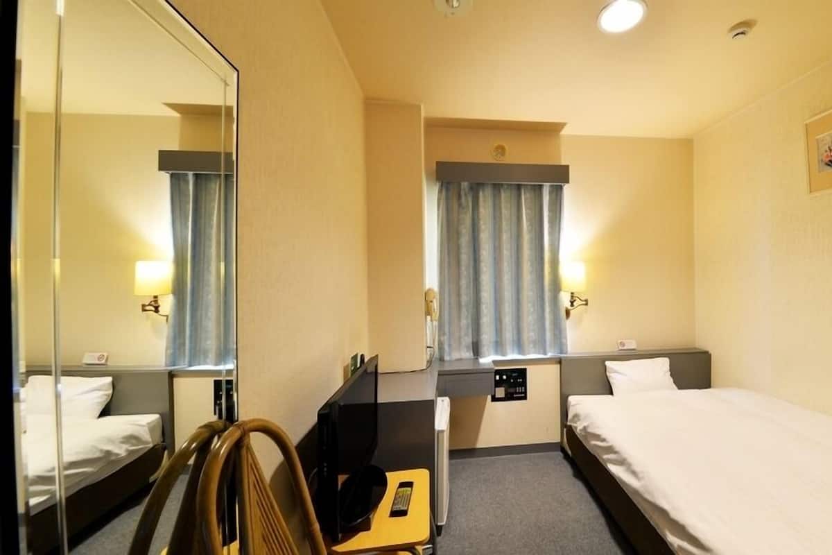 A hotel room with two beds, a desk, a chair, a mirror, a window with curtains, and a wall-mounted light.