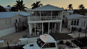 A boat docked at a marina with a house featuring a balcony and outdoor furniture. - Beautiful Ocean view with 35' private seawall, 80' Heated Pool, Hottub (Cudjoe Key)