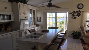 A kitchen with white cabinets, a microwave, and a ceiling fan. There is a dining area with a table and chairs. - Beautiful Ocean view with 35' private seawall, 80' Heated Pool, Hottub (Cudjoe Key)