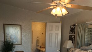 A bedroom with a bed, a ceiling fan, a nightstand, a lamp, and a door leading to a bathroom. - Beautiful Ocean view with 35' private seawall, 80' Heated Pool, Hottub (Cudjoe Key)