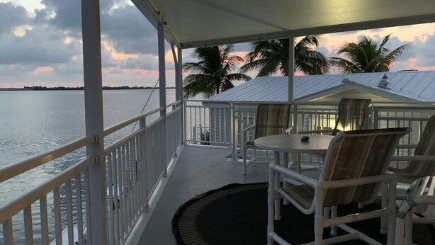 A covered outdoor area with a table and chairs, overlooking a body of water and palm trees. - Beautiful Ocean view with 35' private seawall, 80' Heated Pool, Hottub (Cudjoe Key)