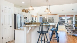 A kitchen with white cabinets, a stainless steel refrigerator, a granite countertop, and two bar stools. - Bluebird: Saltwater Pool, Hot Tub. Golf Community (Corolla)