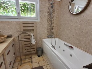 Une salle de bain avec une baignoire, une douche, une fenêtre donnant sur les arbres, un porte-serviettes et une poubelle.