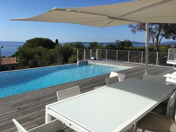 Zona junto a la piscina con una mesa y sillas, piscina y vista al mar.