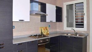 A compact kitchen with dark cabinets, a gas stove, and a window with blinds. - 2 bedroom apartment in agadir (Agadir)